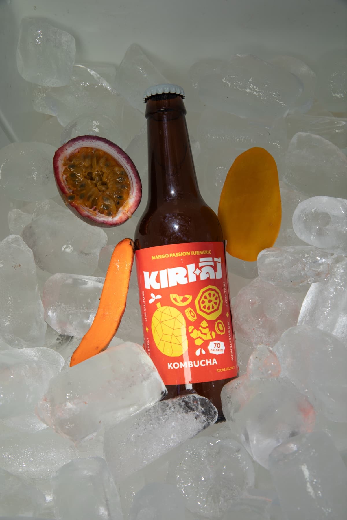 Kiri Kombucha mango passion turmeric bottle on ice with fresh fruit